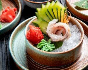 side view of marinated herring fillets with sliced cucumbers ginger and wasabi sauce on ice cubes in a plate on the table